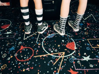 Two people standing on a patterned carpet wearing striped socks and sneakers