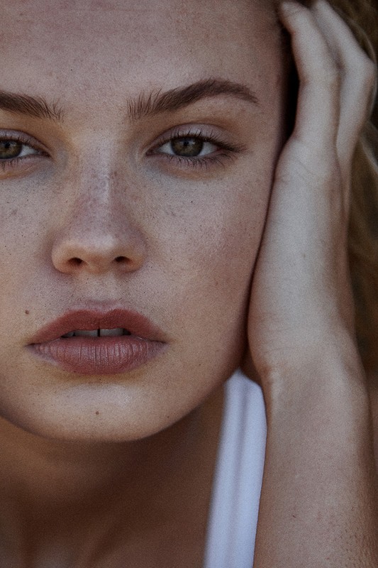 Close-up portrait of a young adult female with fair skin and freckles. The focus is on her face and natural beauty in soft, diffused light.
