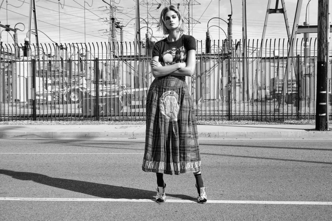 Model standing outdoors with arms crossed wearing a graphic t-shirt and plaid midi skirt in Los Angeles.