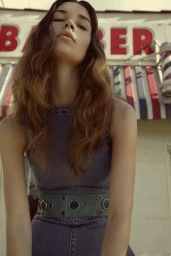 Low-angle shot of a woman with long wavy brown hair wearing a denim dress and studded wide belt outdoors.
