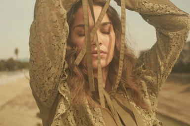 Close-up of a woman in an olive green lace blouse holding fabric ribbons across her face with eyes closed.