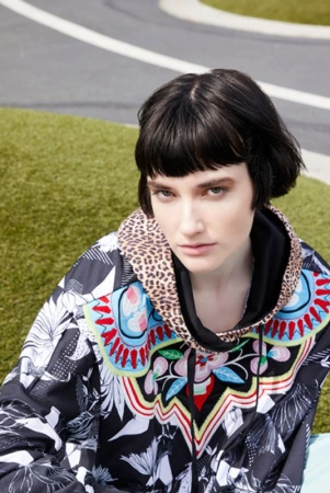 Young woman with short dark hair poses in an outdoor setting wearing a patterned hoodie with a leopard-print hood.