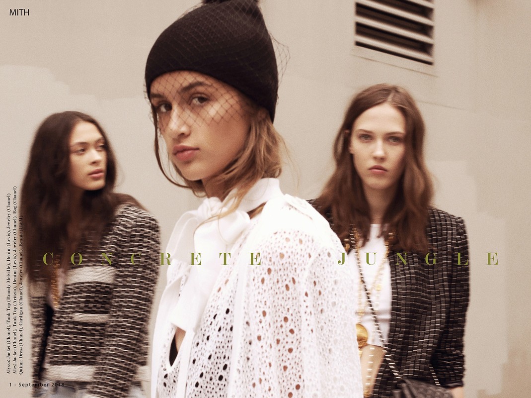 Three women pose in an urban fashion editorial. The model in the foreground wears a black hat and white knit top. Concrete Jungle text overlay.