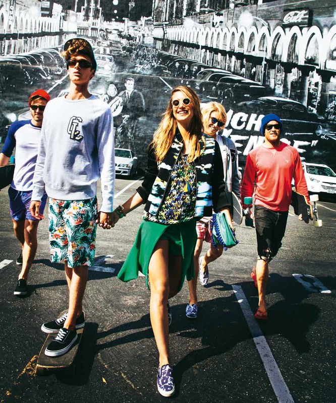 Group of young adults walks across a black asphalt street with white lines in sunny weather.  Street art in the background.