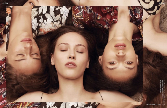 Three women lie with heads close together, creating a symmetrical pattern with faces and floral fabric in a beauty or fashion editorial.