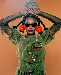 Black woman wearing green floral dress and sunglasses with hands raised above head, styled by Erin Skipley