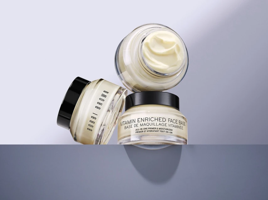 Three jars of Bobbi Brown Vitamin Enriched Face Base arranged on a gray surface, showcasing beauty and skincare product photography.