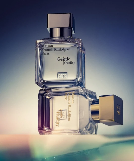 Two Maison Francis Kurkdjian Paris Gentle fluidity perfume bottles stacked with gradient blue background, reflecting light on surface.