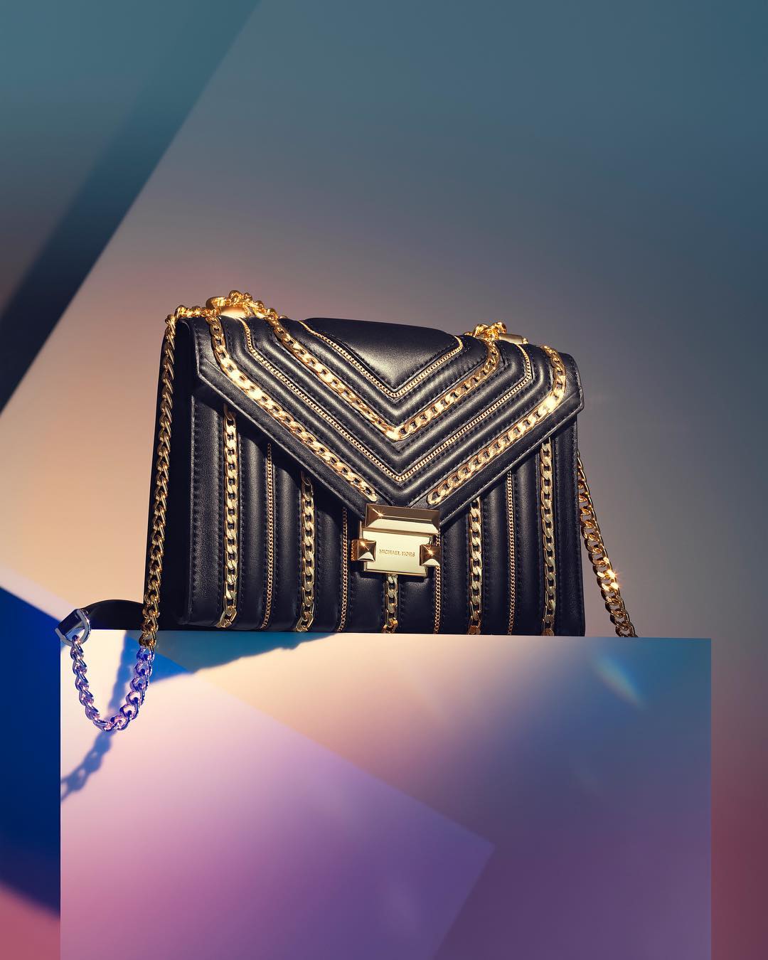 Elegant black leather handbag with gold chain details displayed on a geometric stand, fashion accessory, studio shot.