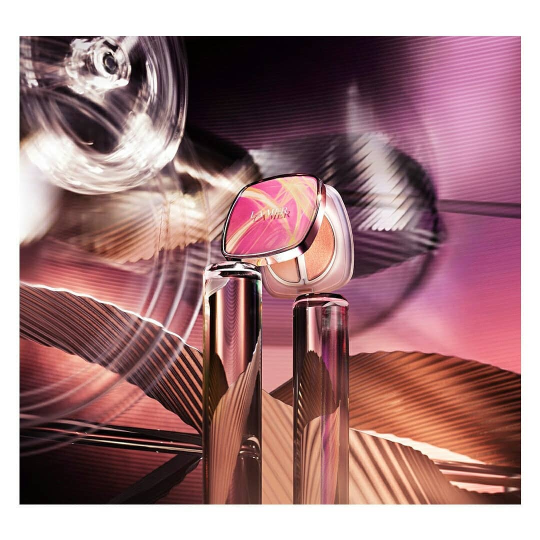 La Mer The Cushion foundation and serum bottle with an abstract light and dark pink background for a beauty and fashion product shot.