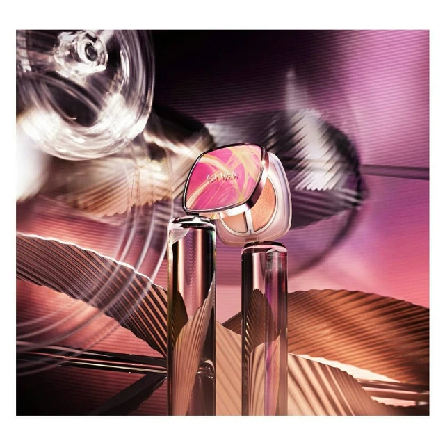 La Mer The Cushion foundation and serum bottle with an abstract light and dark pink background for a beauty and fashion product shot.