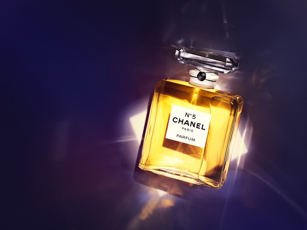 Elegant still life of a perfume bottle against a dark background with light flares, showcasing its clear bottle and golden liquid.