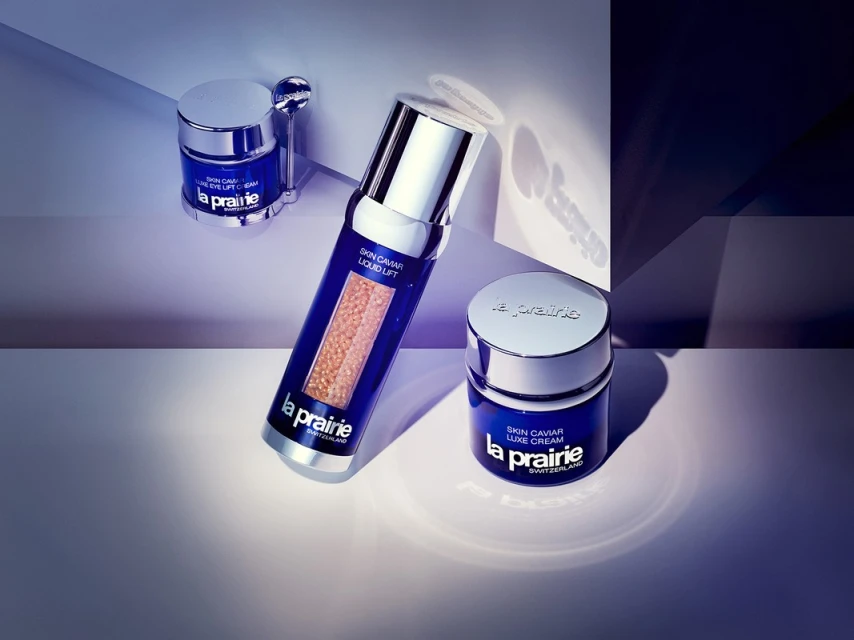 La Prairie Skin Caviar collection: eye lift cream, liquid lift, and luxe cream, set against a purple and white background.