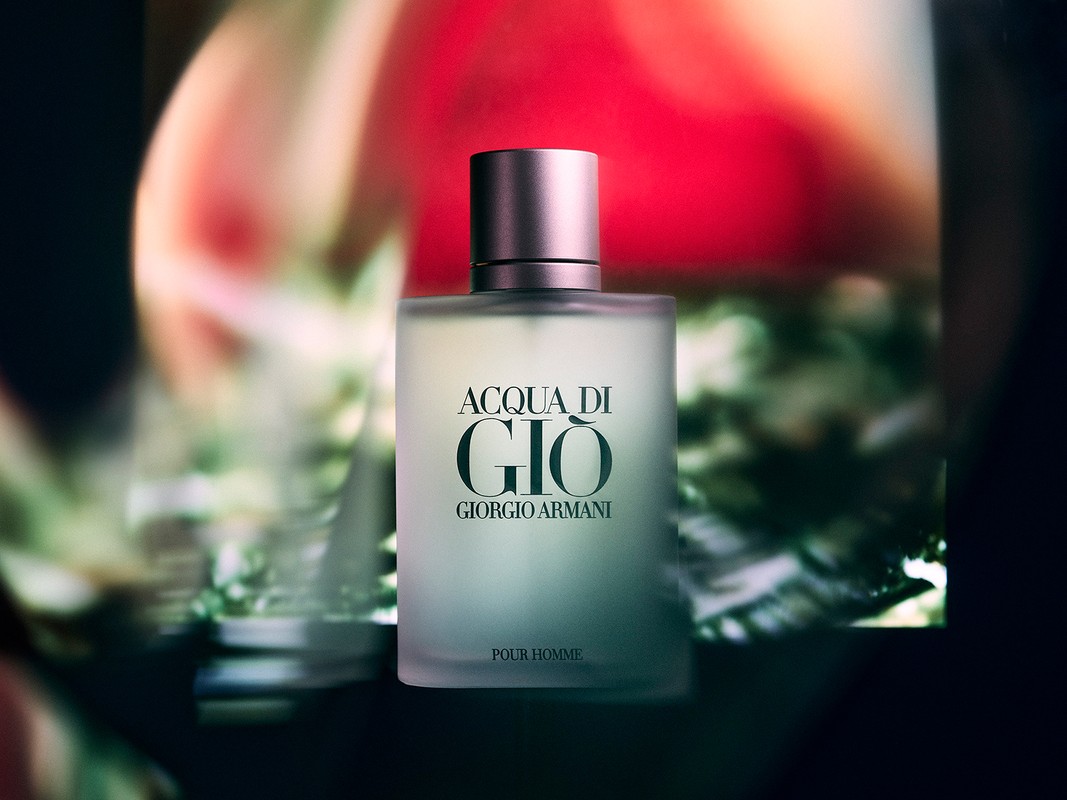Giorgio Armani Acqua Di Gio fragrance bottle against a blurred backdrop featuring red and green hues, presented in a close-up shot.