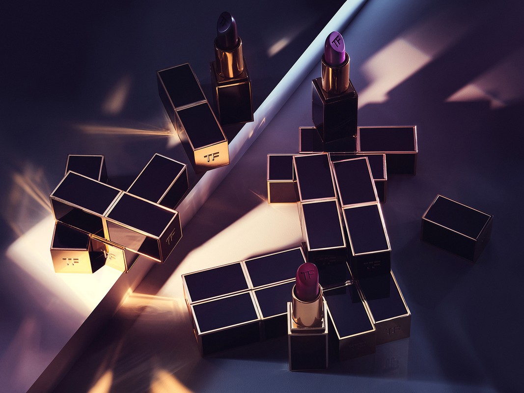Still life of Tom Ford lipsticks in black and gold cases, arranged geometrically on a surface with linear light and shadow.