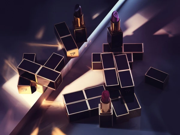 Still life of Tom Ford lipsticks in black and gold cases, arranged geometrically on a surface with linear light and shadow.