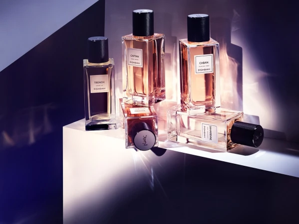 Five glass perfume bottles with black caps arranged on a white podium under dramatic angular lighting.