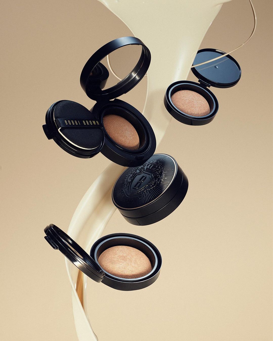 Floating beauty product still life. Black compacts with light powder on a beige background with cream swirl. Minimalist beauty product photography.