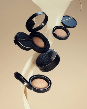 Floating beauty product still life. Black compacts with light powder on a beige background with cream swirl. Minimalist beauty product photography.