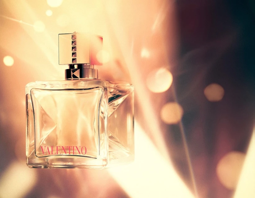 Close-up of a clear glass Valentino perfume bottle with a studded cap against a golden bokeh background, beauty and fragrance.