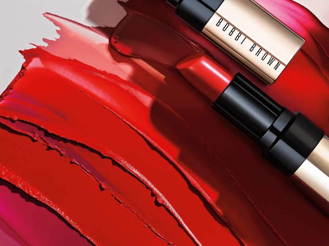 Close-up shot of red lipstick smears and two tubes of Bobbi Brown lipstick. The background is a light gray. Cosmetics concept.