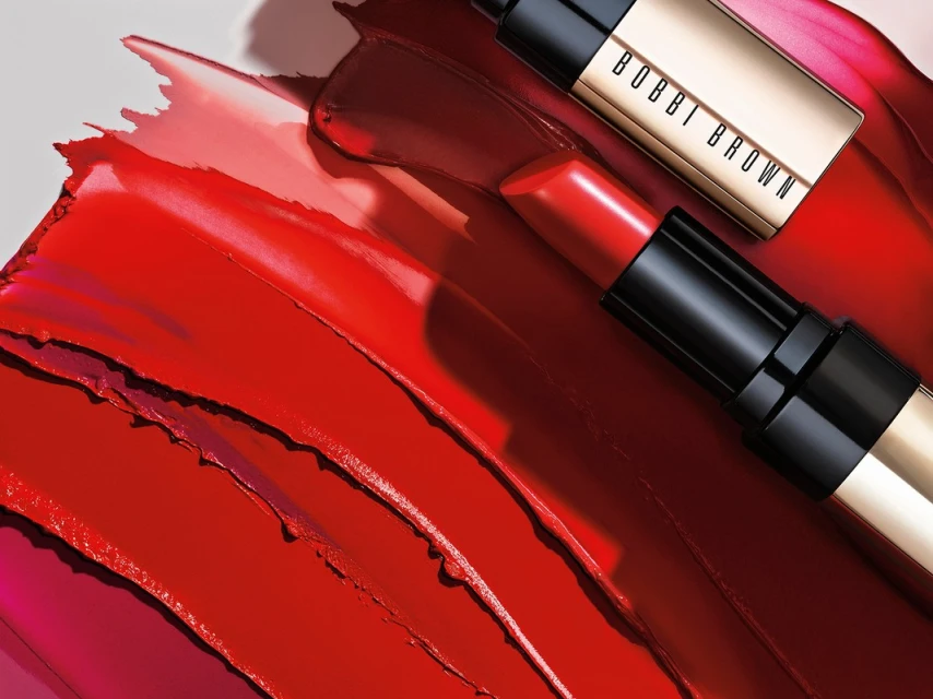 Close-up shot of red lipstick smears and two tubes of Bobbi Brown lipstick. The background is a light gray. Cosmetics concept.