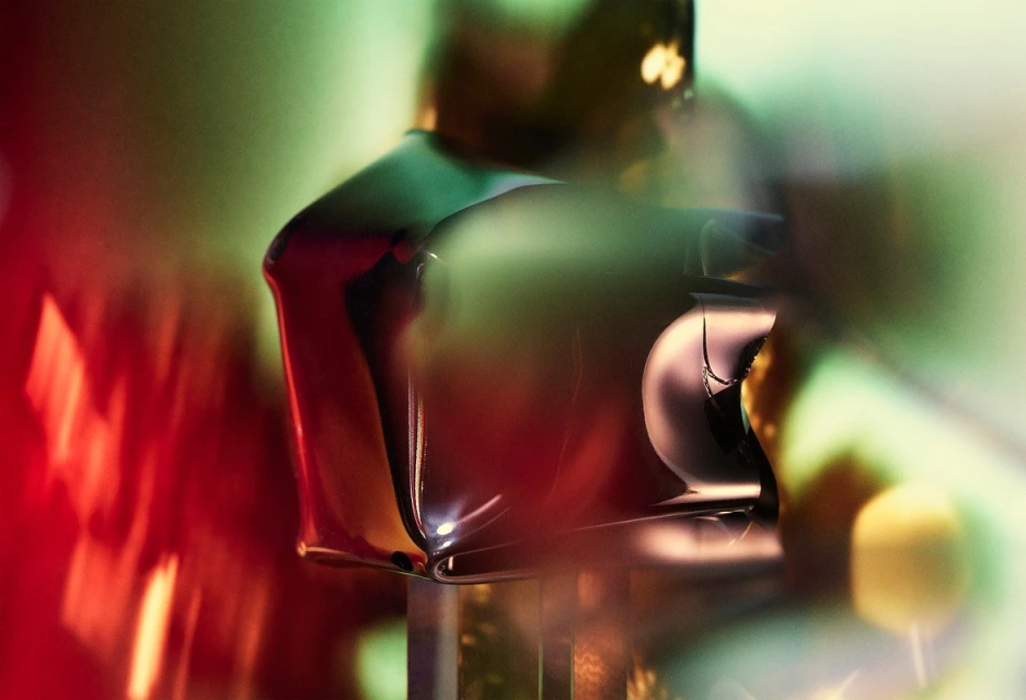 Abstract close-up of shiny, dark red geometric forms with blurred green and yellow light patterns in the background, creating a surreal scene.