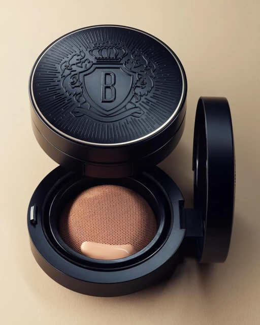 Beauty product shot of a black compact container of face powder with a beige applicator visible, set against a light beige backdrop.
