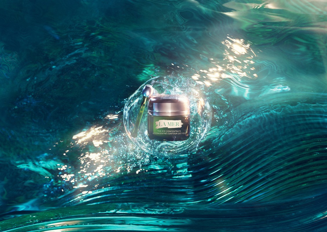 La Mer eye concentrate cream jar with applicator, floating in water with light reflections, on a teal and turquoise background.