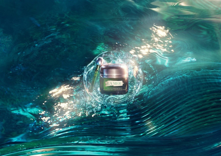 La Mer eye concentrate cream jar with applicator, floating in water with light reflections, on a teal and turquoise background.