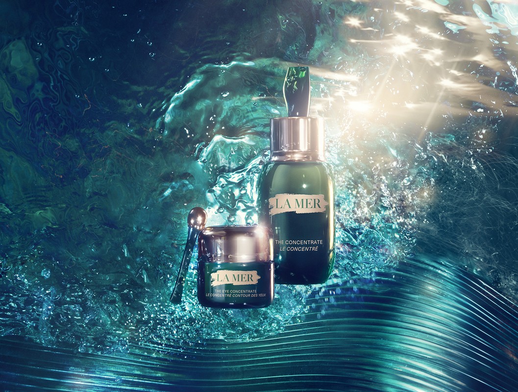 La Mer skincare products, including serum and eye concentrate, sit against a textured, turquoise water-like background with bright lighting.