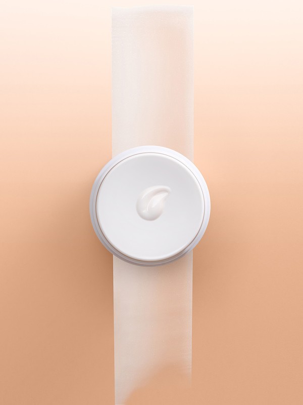 Overhead studio shot of a white cream jar and product on a white surface with an peach gradient background for beauty advertising.
