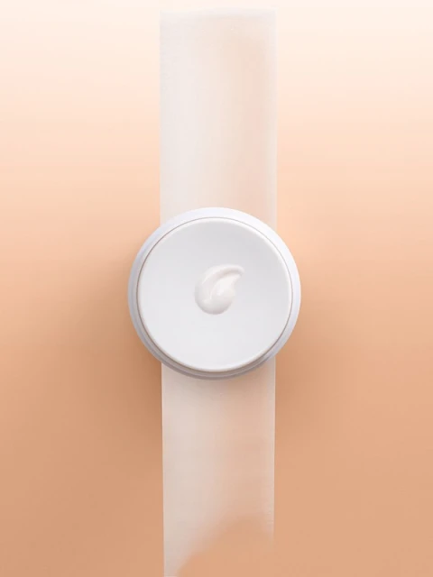 Overhead studio shot of a white cream jar and product on a white surface with an peach gradient background for beauty advertising.