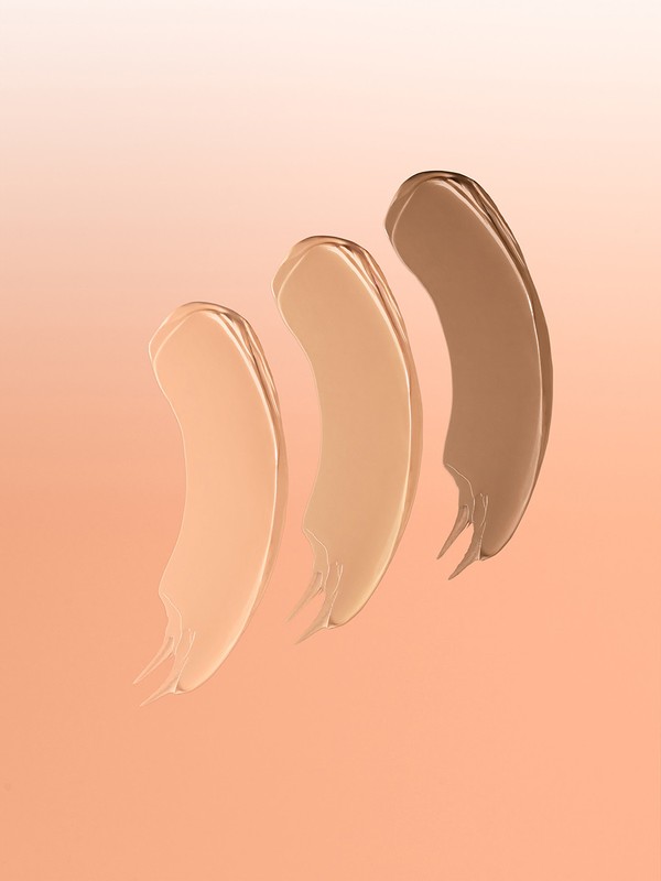 Three swipes of different shades of foundation make-up are displayed against an orange gradient background for beauty product presentation.