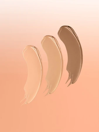 Three swipes of different shades of foundation make-up are displayed against an orange gradient background for beauty product presentation.