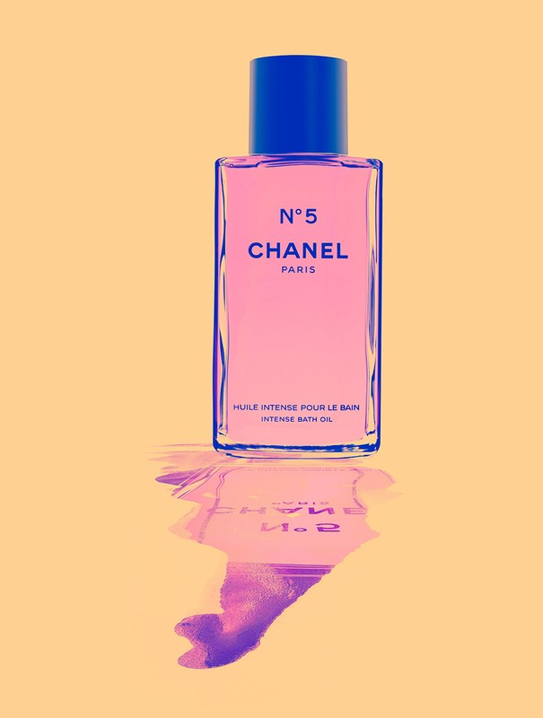 Chanel N°5 Intense Bath Oil bottle on orange background with reflection, showcasing its pink liquid and blue accents.