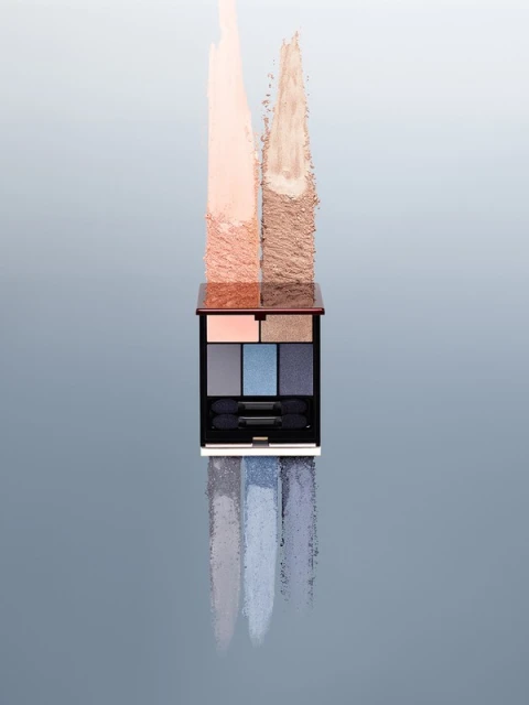 Eye shadow palette with swatches in neutral and blue tones, makeup product shot on a reflective surface against a gradient backdrop.