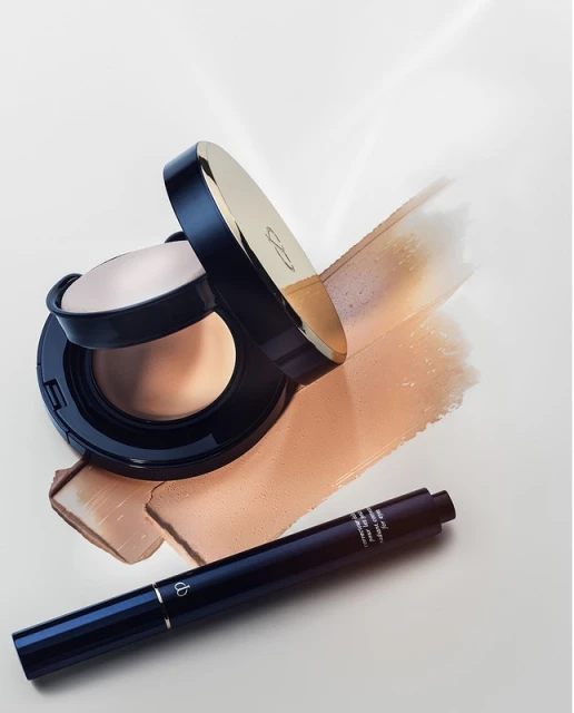 Close-up studio shot of makeup foundation compact with applicator and concealer stick on bright background with foundation smears.