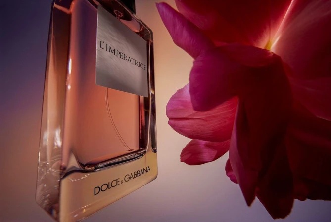Close-up of a Dolce and Gabbana fragrance bottle titled L'Imperatrice next to a vibrant pink flower petal.