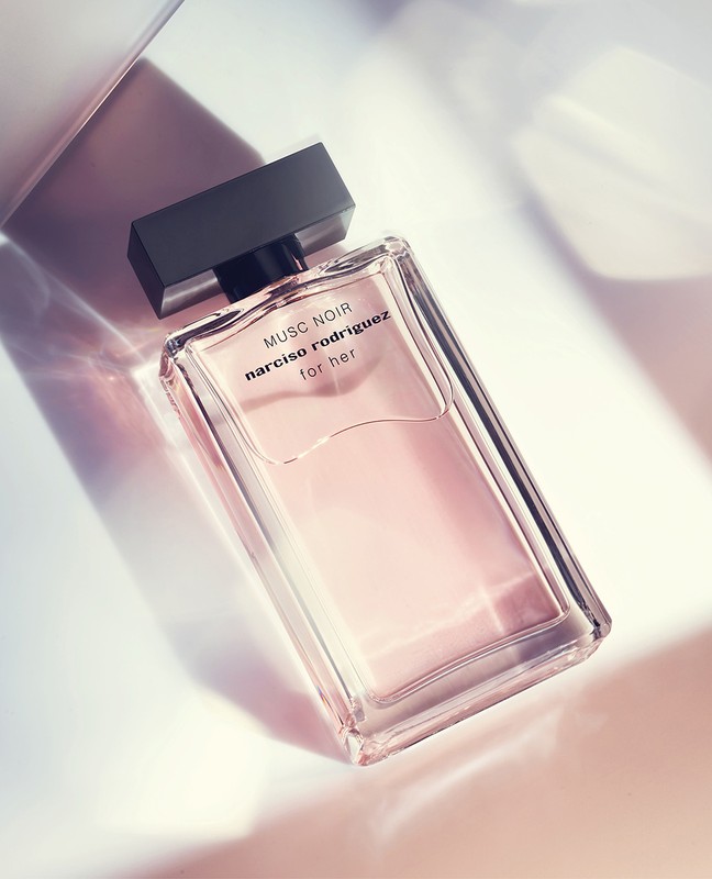 Rectangular clear glass perfume bottle with black cap labeled 'Musc Noir Narciso Rodriguez for her' on a gradient light background.