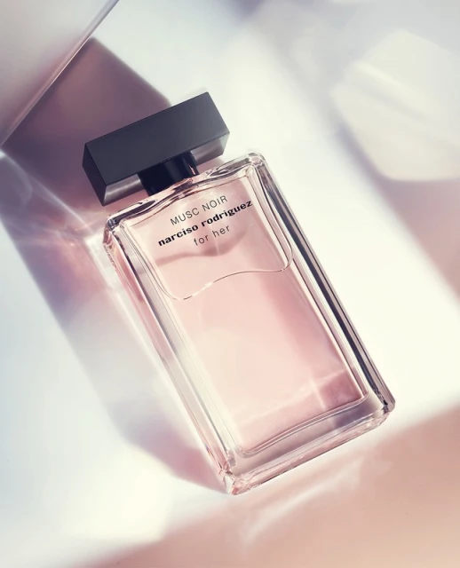 Rectangular clear glass perfume bottle with black cap labeled 'Musc Noir Narciso Rodriguez for her' on a gradient light background.