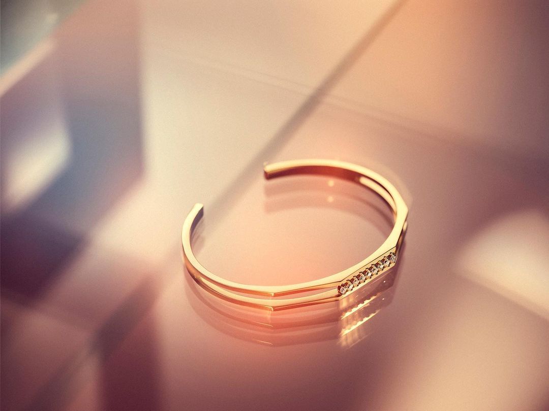 Close up of a gold cuff bracelet with small embedded diamonds resting on a reflective surface