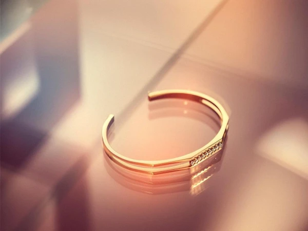 Close up of a gold cuff bracelet with small embedded diamonds resting on a reflective surface