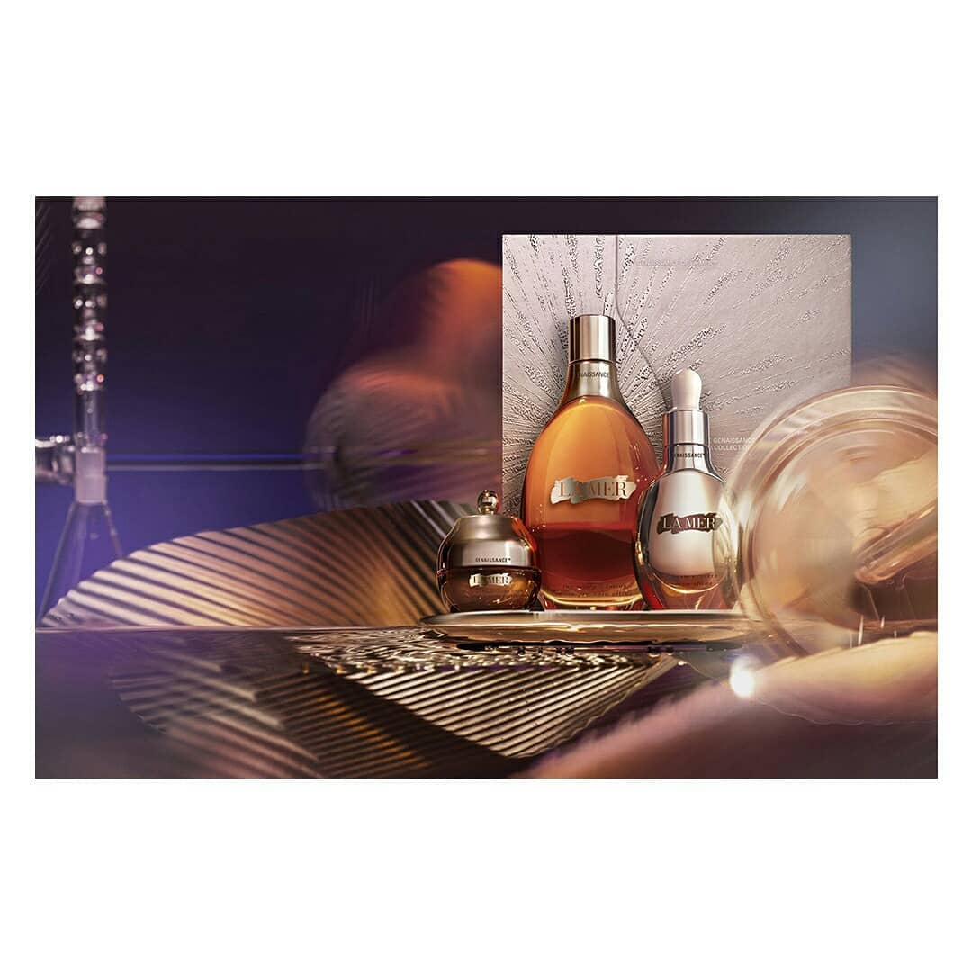Amber-toned beauty products including bottled fragrance and moisturizer on a reflective gold surface in a staged studio shot.
