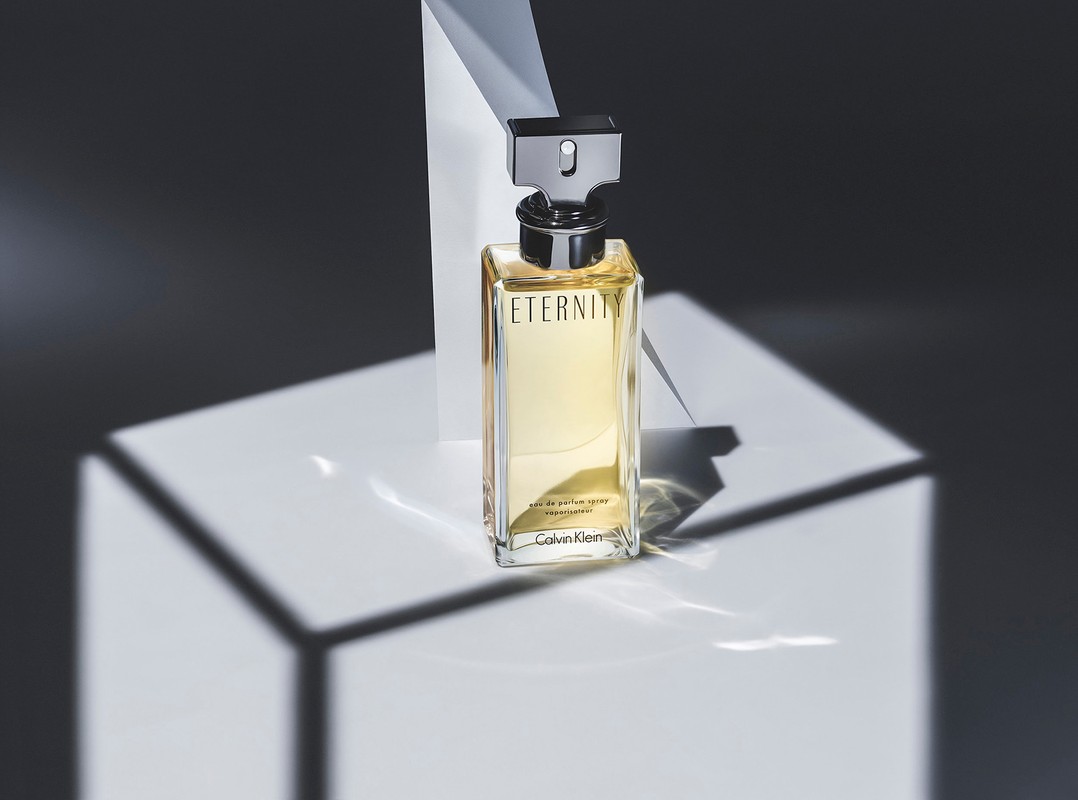 Eternity Eau de Parfum spray by Calvin Klein on a white geometric pedestal with grey and white background and shadows. 
