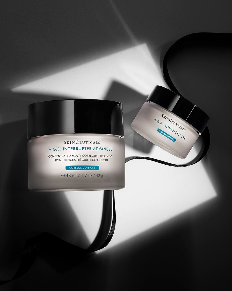 Two jars of Skinceuticals A.G.E. Interrupter Advanced cream sit with a black ribbon on a surface in a studio with artificial lighting.
