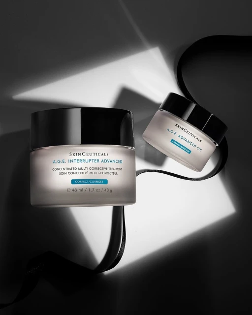 Two jars of Skinceuticals A.G.E. Interrupter Advanced cream sit with a black ribbon on a surface in a studio with artificial lighting.