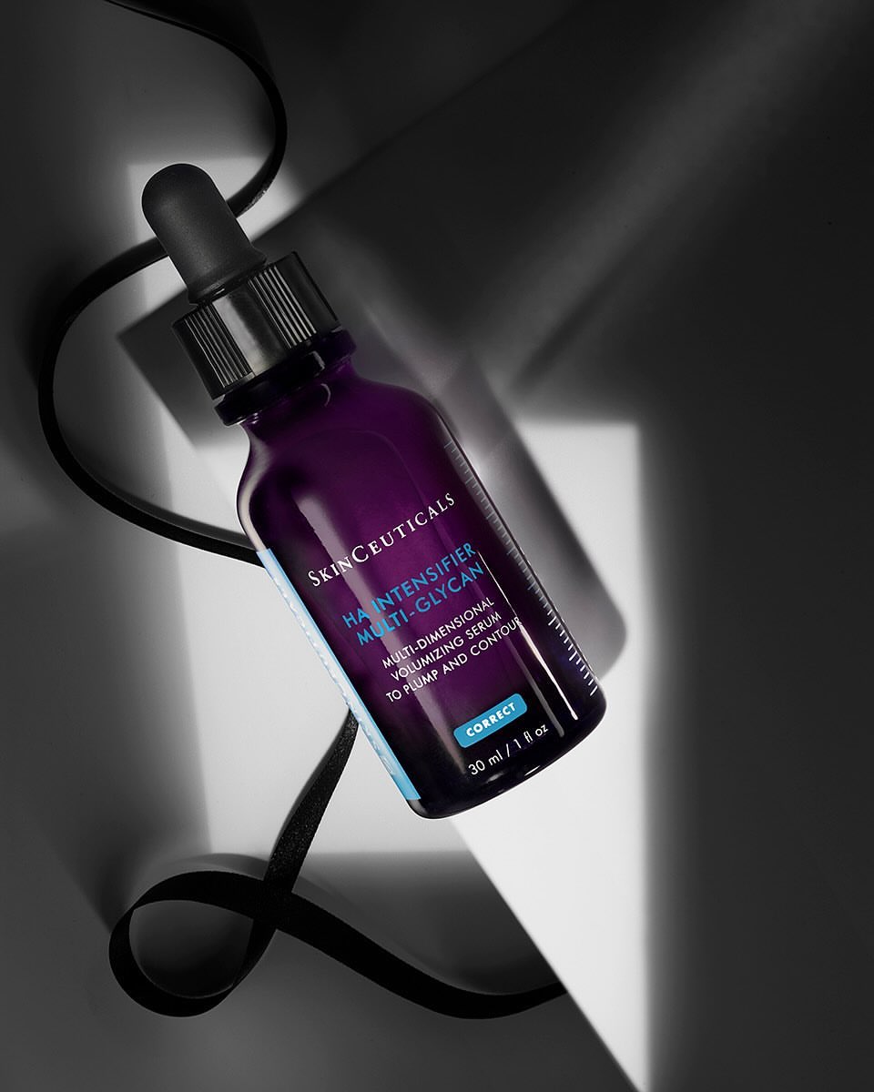 Close-up of a purple glass bottle with a black dropper, showcasing a skin care product against a contrasting light and dark background.