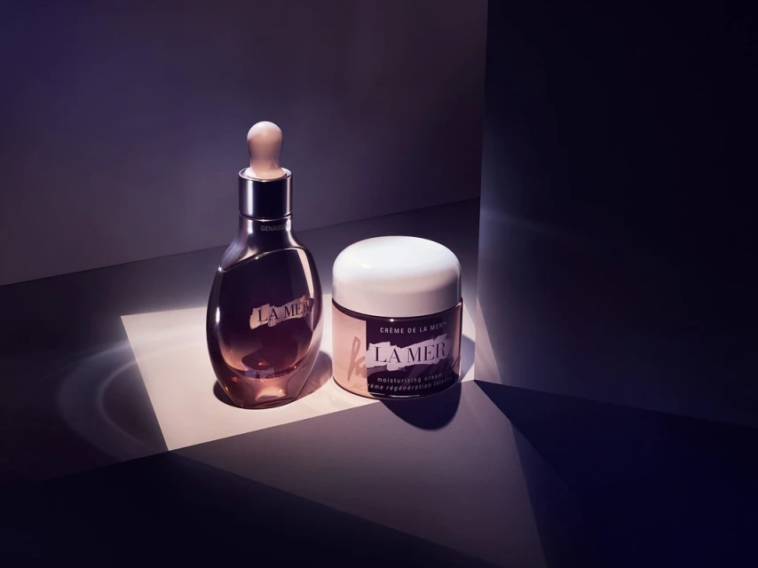 La Mer skincare products, serum and moisturizing cream, showcased with sleek packaging and contrasted lighting against a dark backdrop.