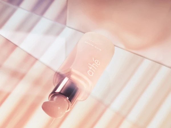 Close-up of a frosted pink 'athé Glow Master Vegan Collagen Boosting Serum' bottle with silver pump on a light pink striped surface.